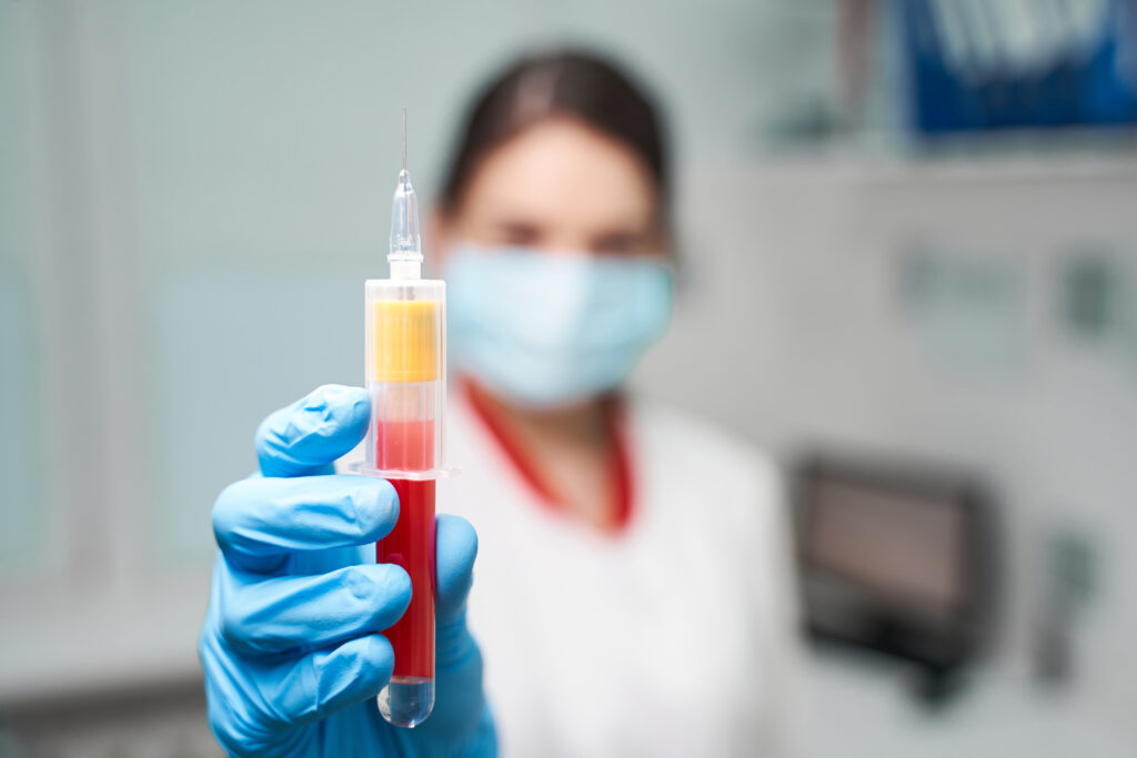 Young brunette girl working in clinic, wearing rubber gloves while taking sample of blood