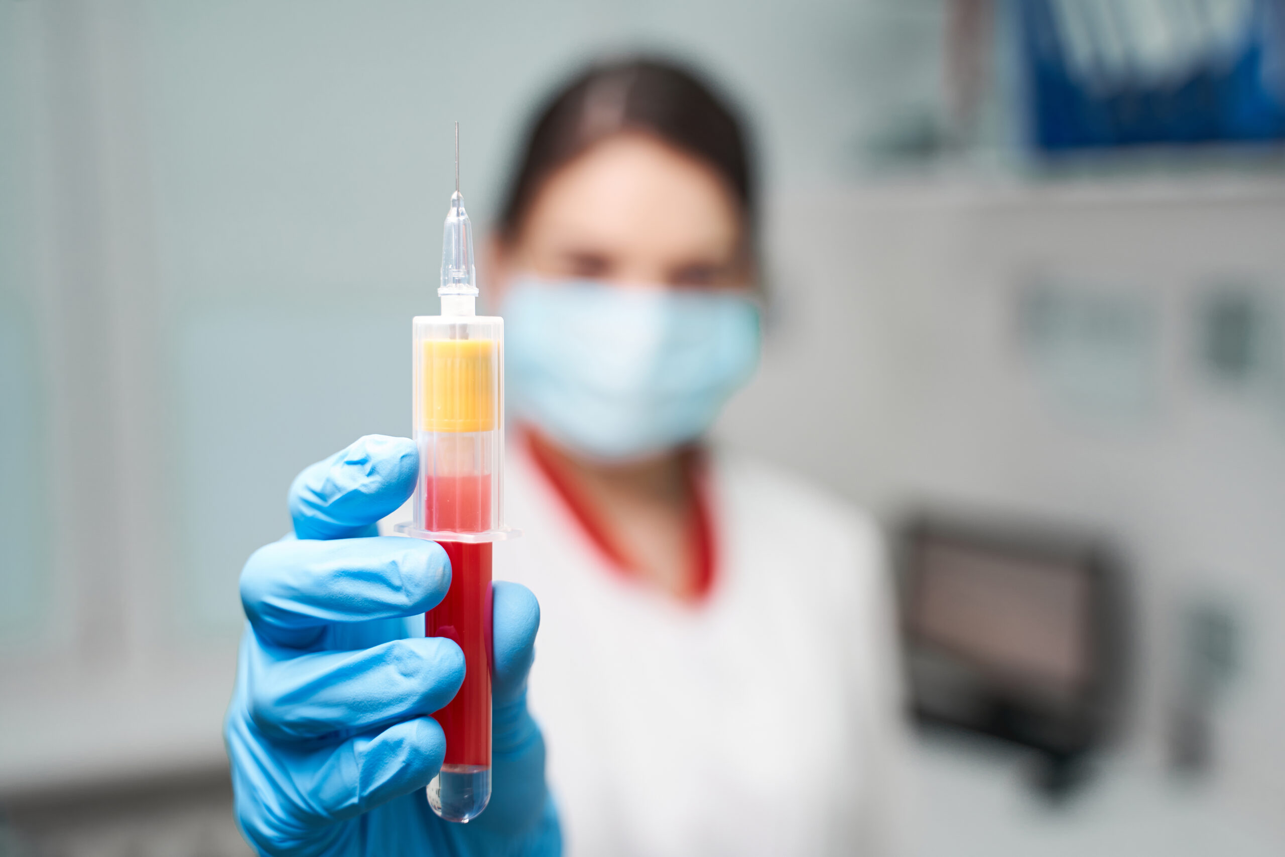 Young brunette girl working in clinic, wearing rubber gloves while taking sample of blood