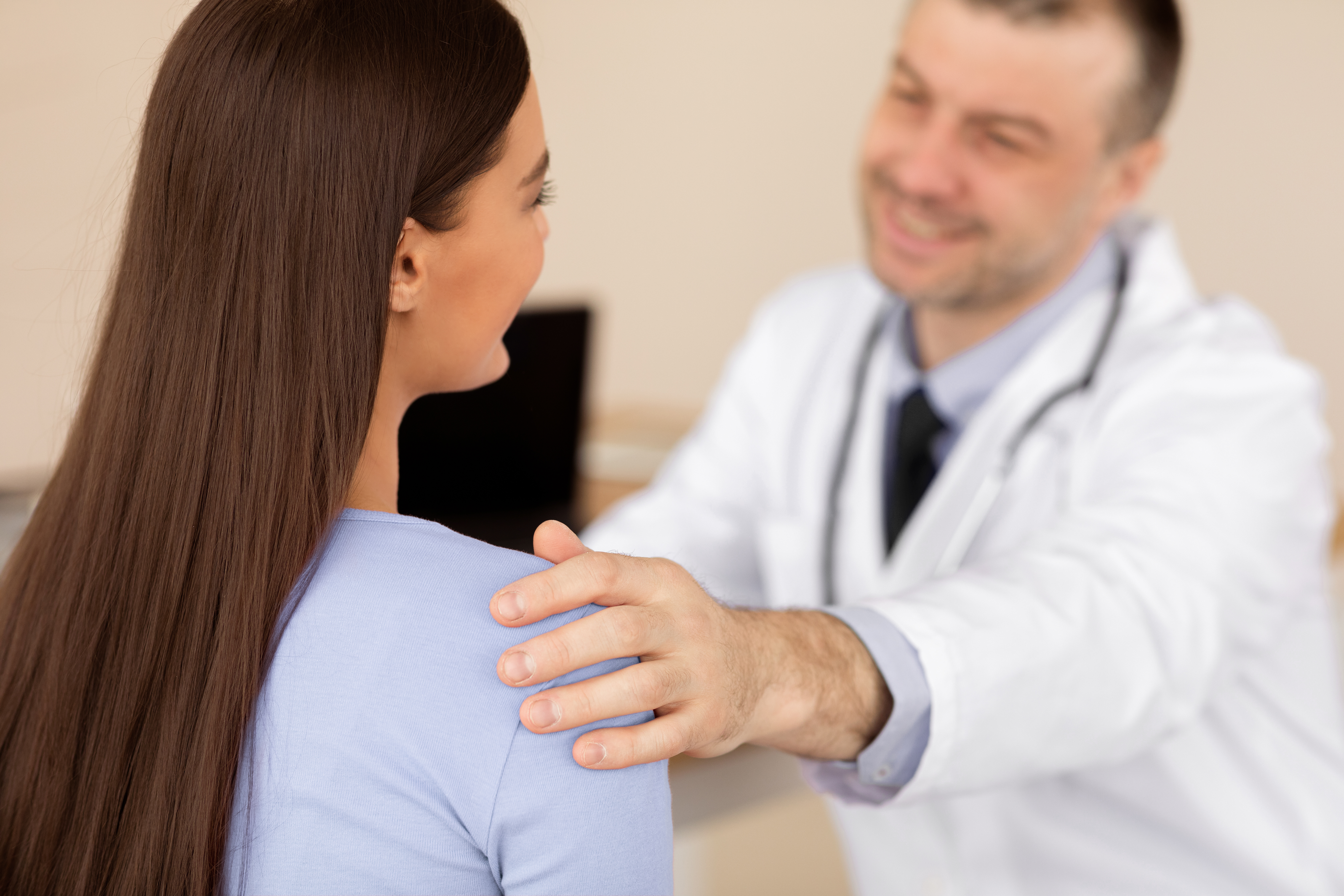 Mature male specialist supporting young female in clinics, touching her shoulder