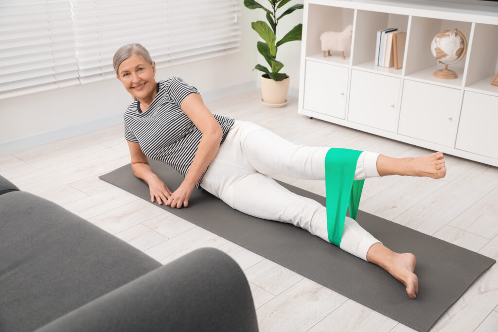 Senior woman doing exercise with fitness elastic band on mat at home