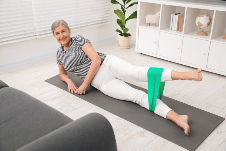 Senior woman doing exercise with fitness elastic band on mat at home