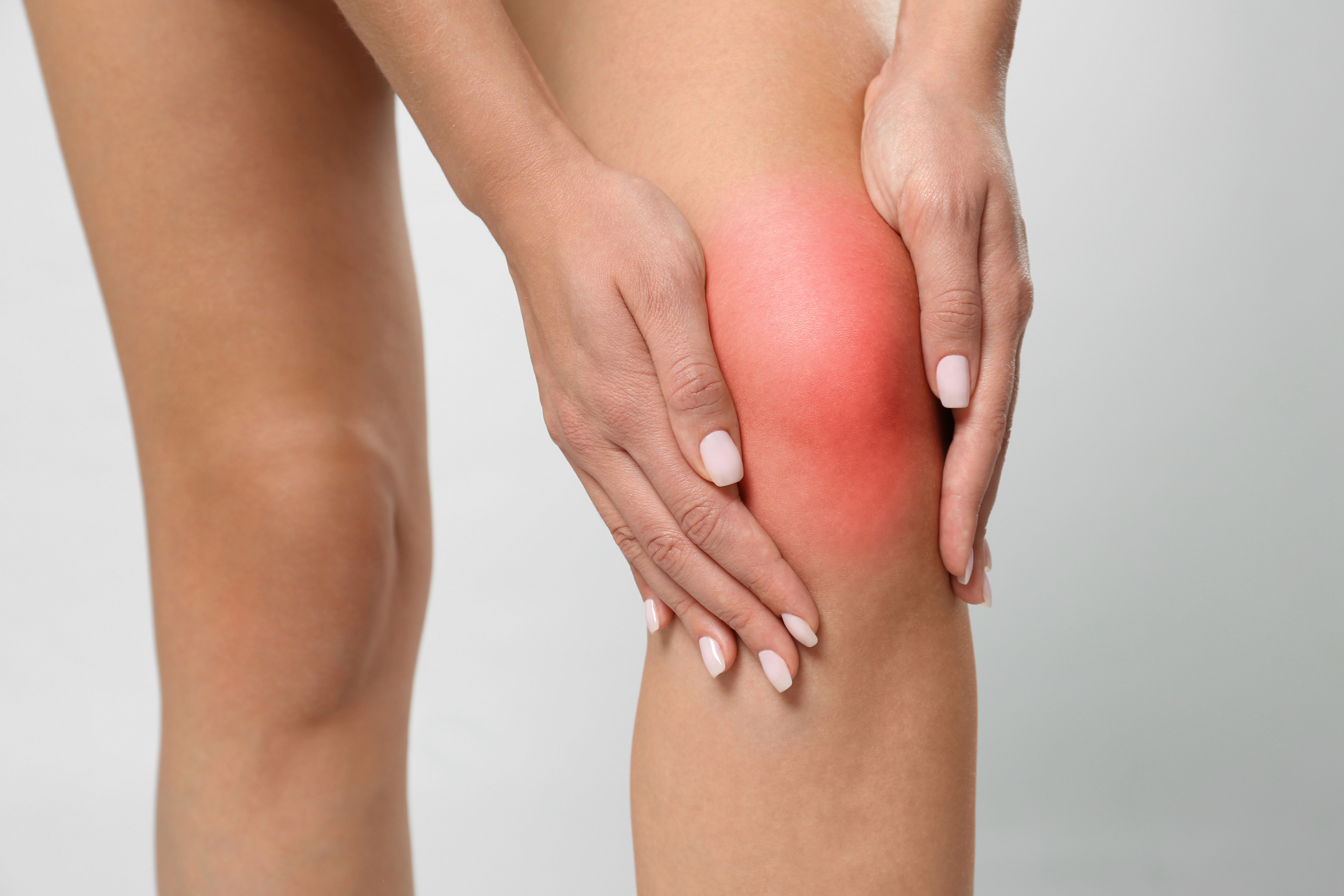 Woman having knee problems on grey background, closeup